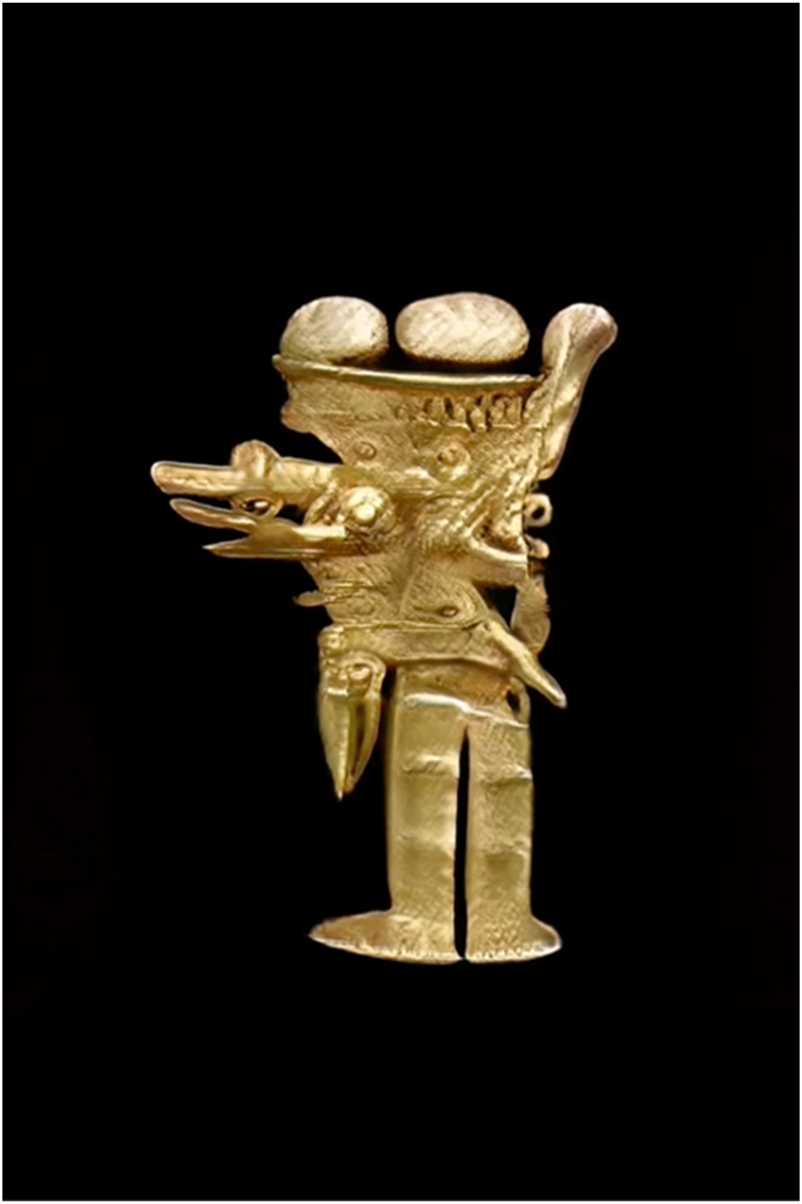 A gold artifact featuring a stylized figure with intricate details, including two prominent spherical forms on top and abstract shapes extending from the sides, set against a black background.
